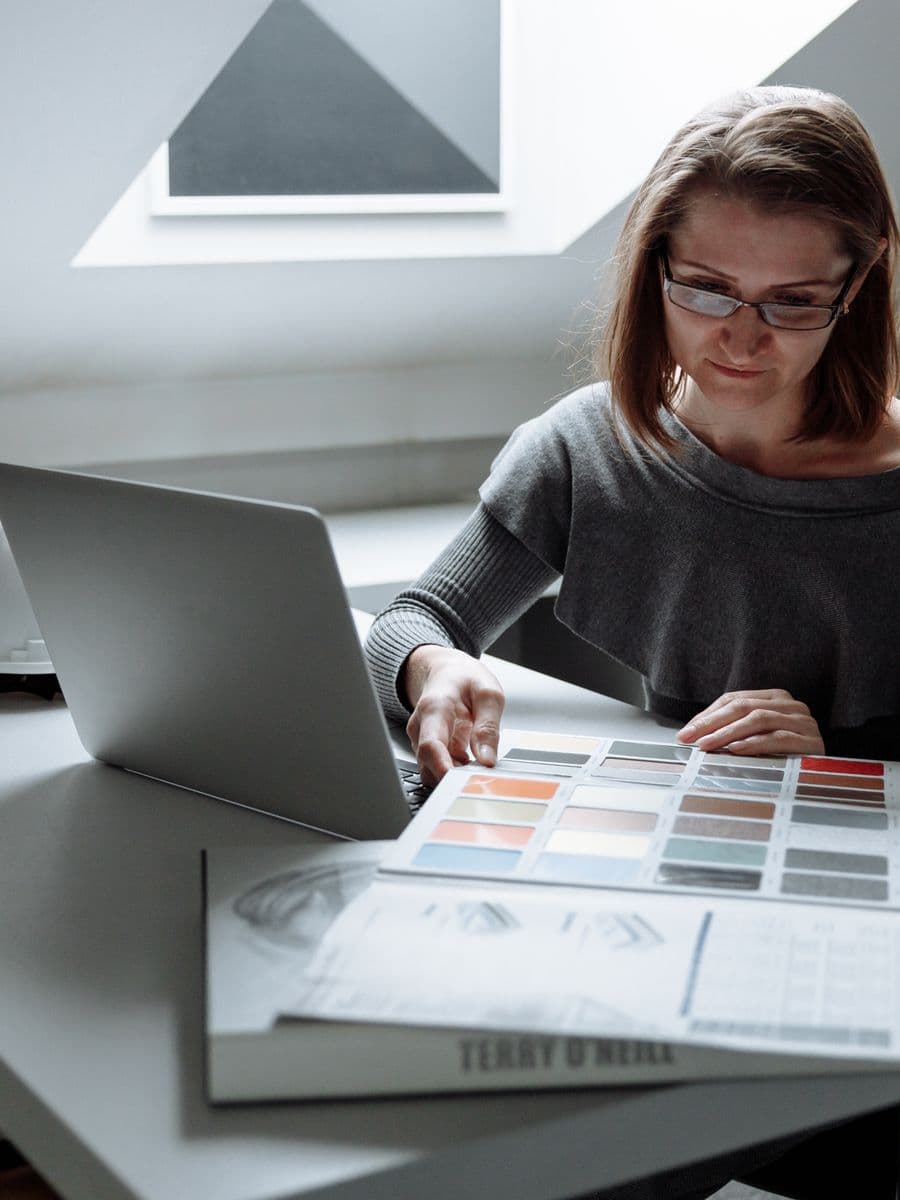 Designer focused at her workspace reviewing work on a laptop